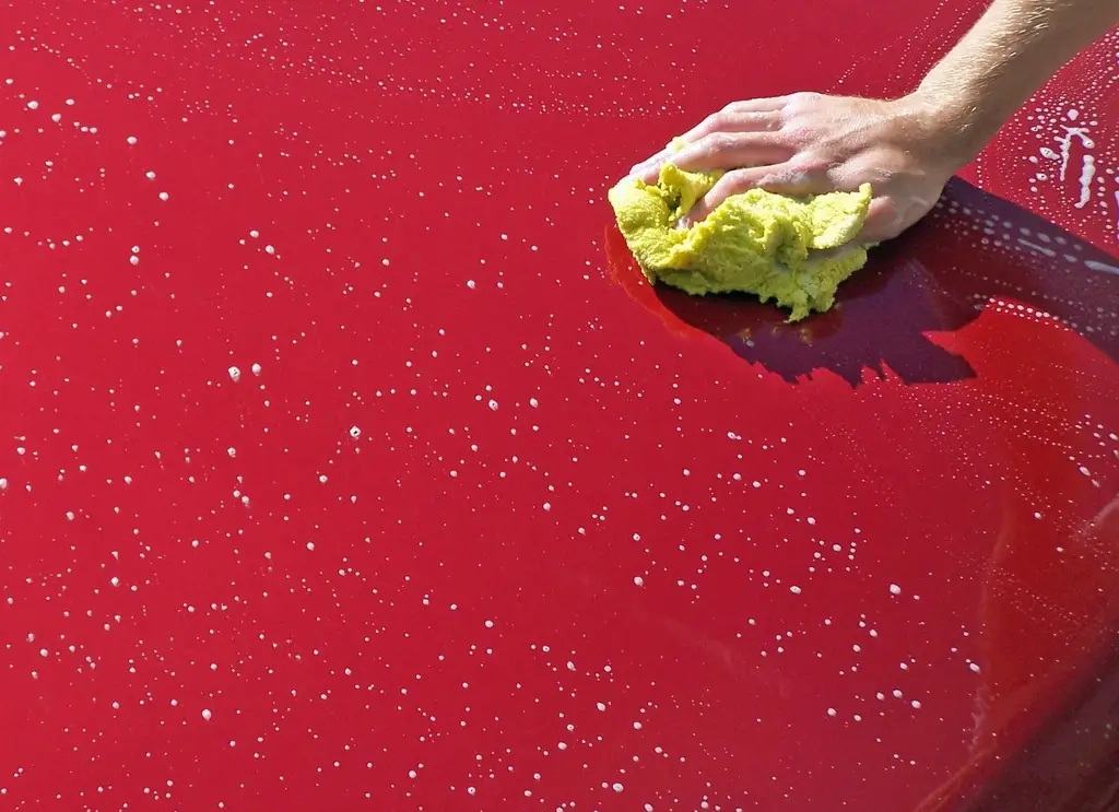 A hand polishing a red car with a yellow cloth